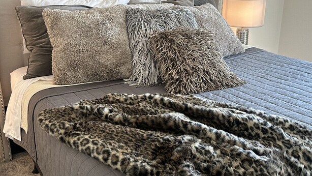 Un lit doté d’une tête de lit capitonnée, de draps gris et d’un plaid à motifs léopard.