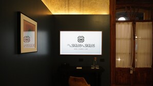 A dark-themed room with a framed picture, a digital display, a wooden desk, and a chair. - Por los Siglos Hotel (Huamantla)
