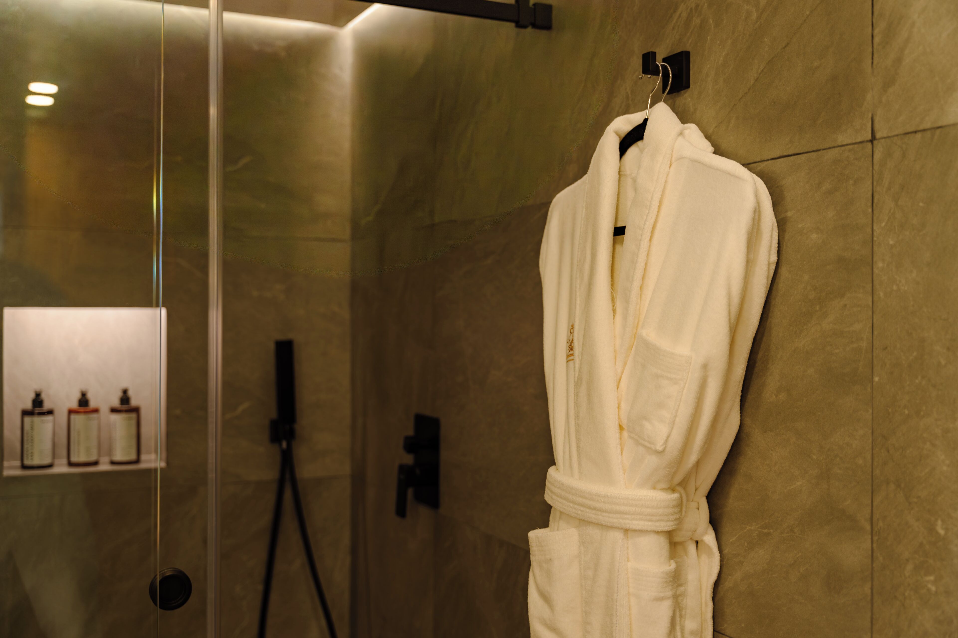 Un baño con cabina de ducha de vidrio, una bata blanca colgada de un perchero y artículos de aseo en un estante.