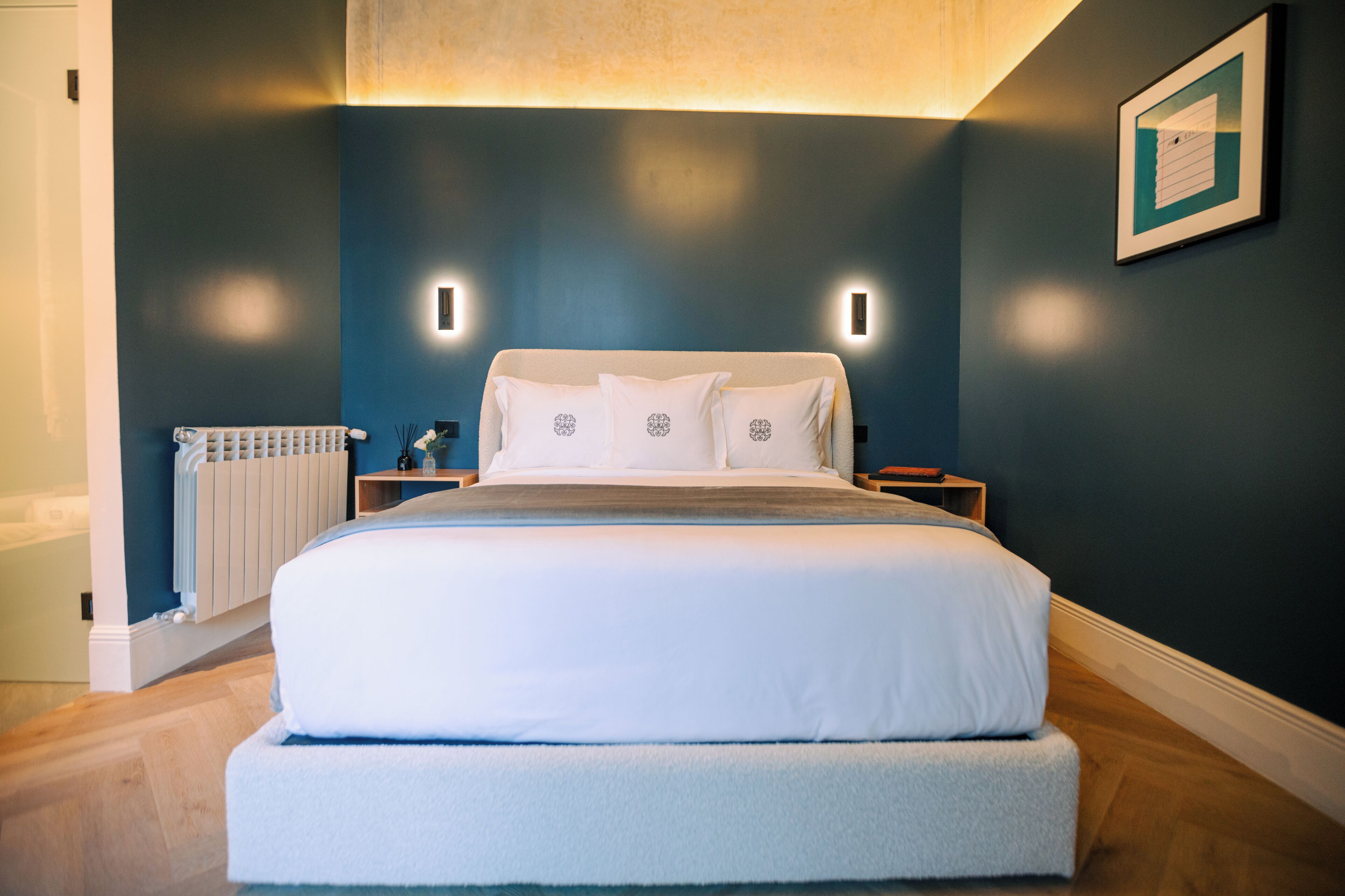 Un dormitorio moderno con una cama grande, mesitas de noche, un radiador y un cuadro enmarcado en la pared.
