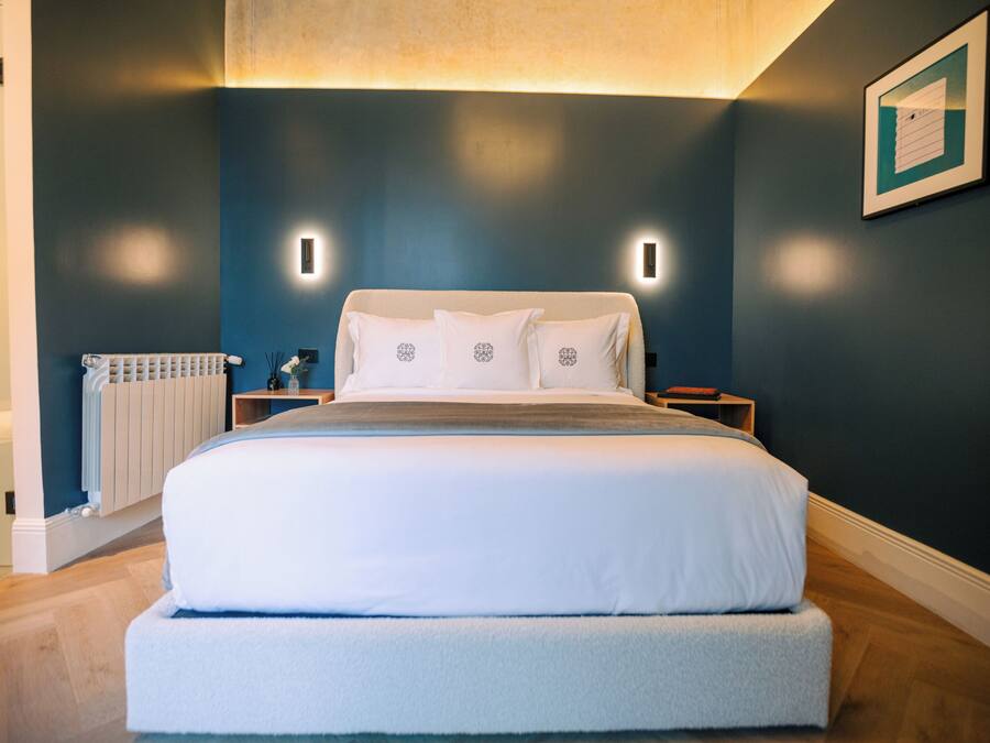 Un dormitorio moderno con una cama grande, mesitas de noche, un radiador y un cuadro enmarcado en la pared.