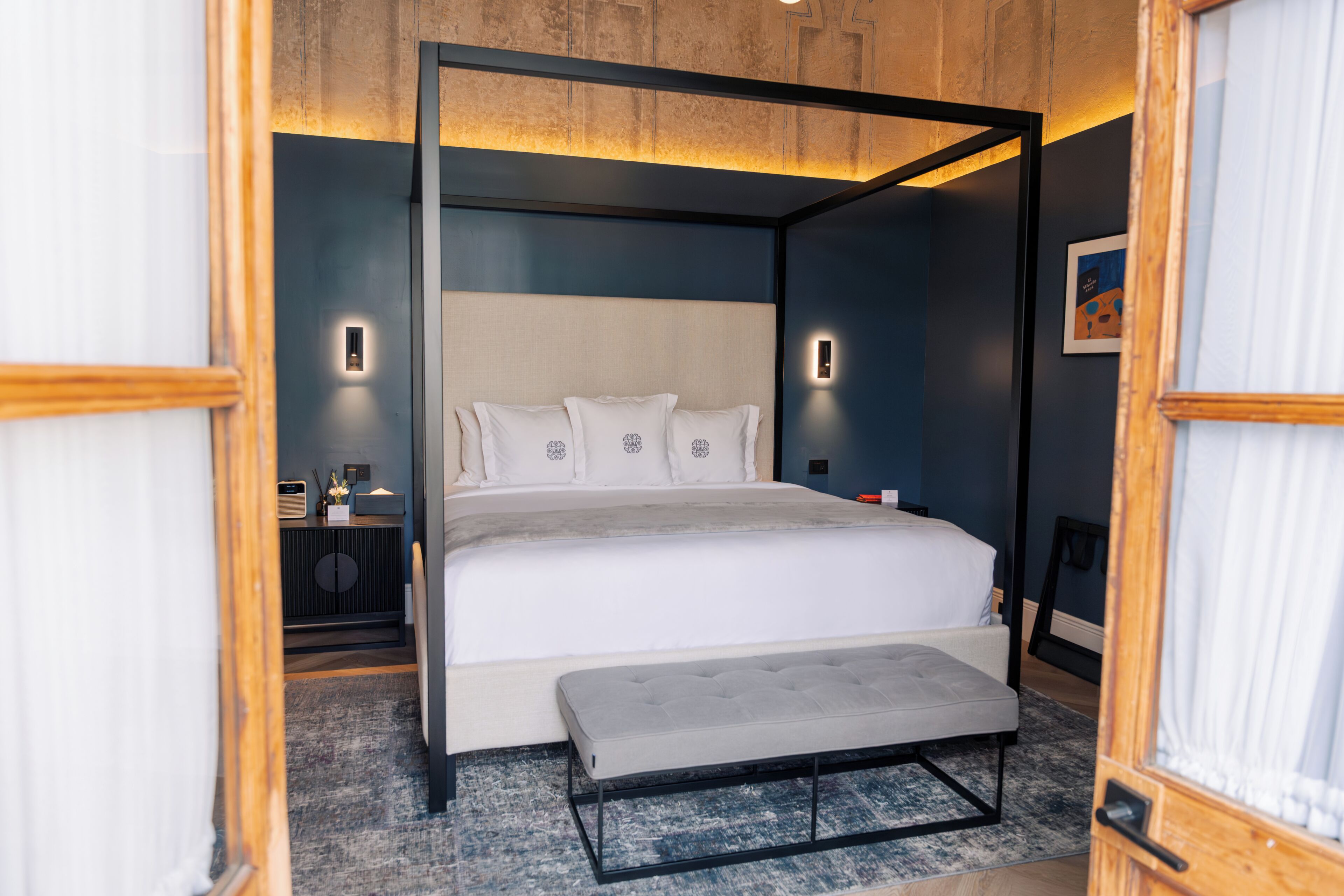Un dormitorio moderno con una cama con dosel, una mesita de noche y un banco.