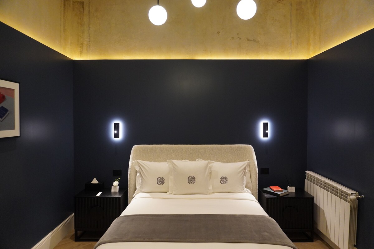 A bedroom with a bed, bedside tables, and wall-mounted lights.