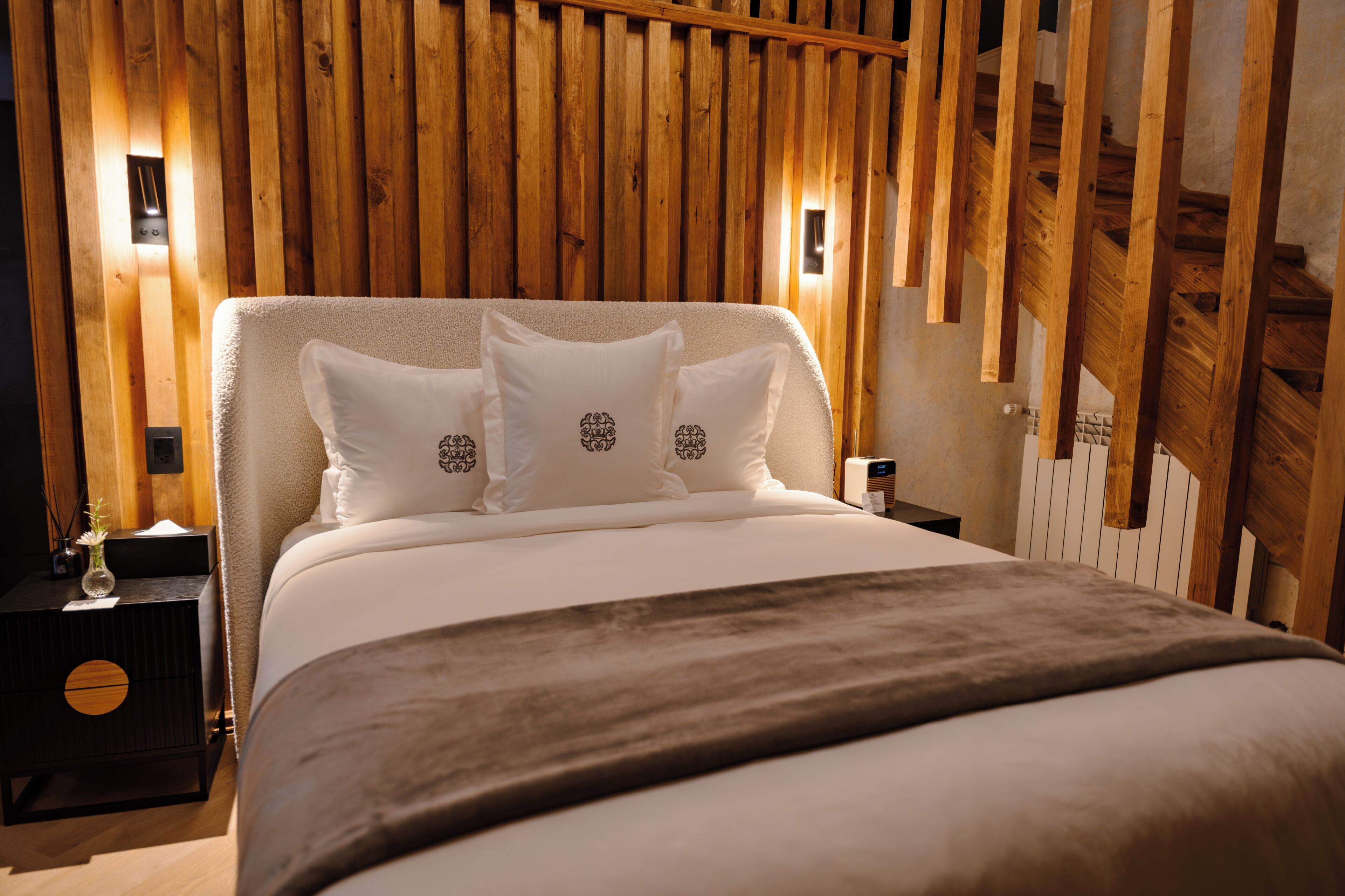 Habitación de hotel con pared de listones de madera, cama con ropa blanca y mesita de noche con lámpara.
