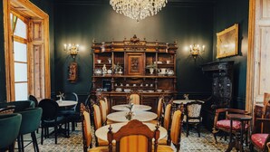 Uma sala de jantar com mesas e cadeiras redondas, um buffet de madeira, arandelas na parede e um lustre.
