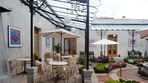 An outdoor patio with round tables and chairs, surrounded by potted plants and a decorative metal pergola. - Por los Siglos Hotel (Huamantla)