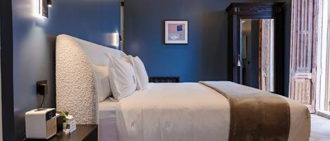 A bedroom with a large bed, a bedside table with a lamp, and a wall-mounted light fixture.