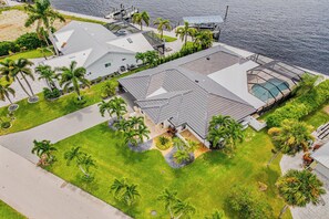 Vista aérea de una casa moderna con un techo amplio, rodeada de palmeras y una piscina.