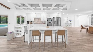 Una cocina amplia con armarios blancos, una isla grande con taburetes de bar y vista a una piscina.