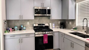 A modern kitchen with grey cabinets, stainless steel appliances, a black stove, and a white countertop. - Stylish 2BR Suite in Vibrant LA Area -> Complimentary WiFi, AC & Parking (Los Angeles)
