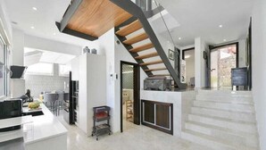 Una cocina moderna con una isla central, un área de comedor con mesa y sillas, y una escalera que sube a un nivel superior.