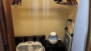 A compact room with a bed, a small heater, a portable fan, and a pet carrier.