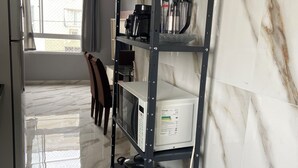 Eine Küche mit Marmor-Spritzschutz, einem Edelstahl-Kühlschrank, einer Mikrowelle und einer schwarzen Regaleinheit mit Töpfen und einem Wasserkocher.