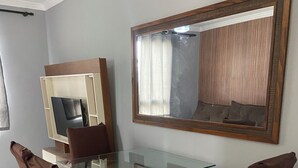 Ein Essbereich mit einem Tisch mit Glasplatte, vier braunen Stühlen, einer Holzkommode mit Fernseher und einem großen Spiegel an der Wand.