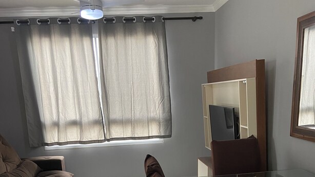 Ein Wohnzimmer mit einem Glastisch, braunen Ledersesseln, einem braunen Sofa, einem Deckenventilator und einem großen Fenster mit Vorhängen.