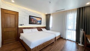 Habitación de hotel con dos camas, piso de madera, pared de ladrillo blanco, un cuadro, una puerta de madera y una ventana con cortinas.