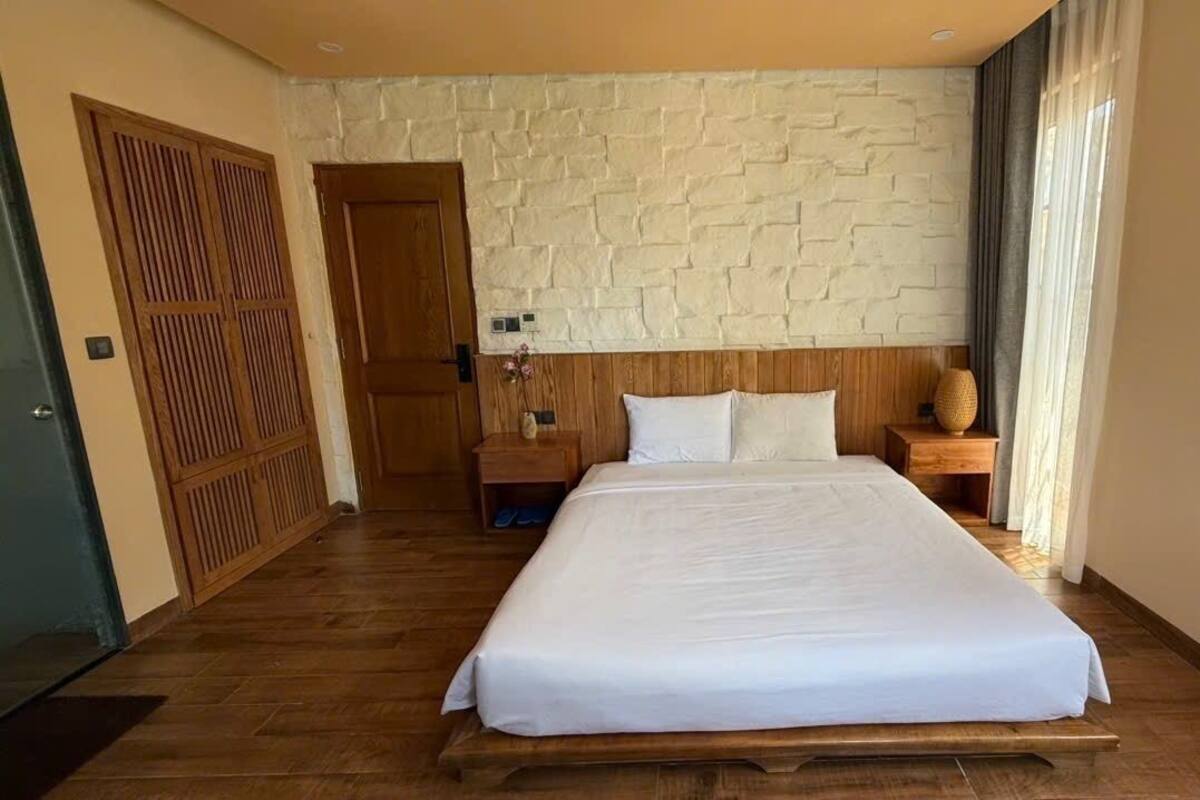 Hotellihuone, jossa on suuri sänky, puinen pääty ja kiviseinä.