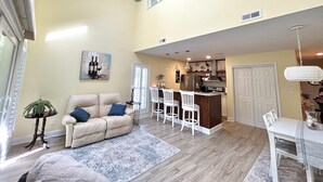 A spacious living area with a high ceiling, a ceiling fan, a dining area with bar stools, and a kitchen with a refrigerator and stove. - 3 Miles from beach. 2-bedroom, 2 bath condo in Little River with 3 beds. (Little River)