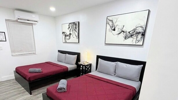 Two single beds with red and grey bedding, a small bedside table with a lamp, and abstract wall art. - Fun in the South and Sun (Hallandale Beach)