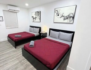 Two single beds with red and grey bedding, a small bedside table with a lamp, and abstract wall art. - Fun in the South and Sun (Hallandale Beach)