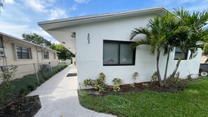 A single-story house with a white exterior, number 303, a small front yard with a palm tree, and a visible security camera. - Fun in the South and Sun (Hallandale Beach)