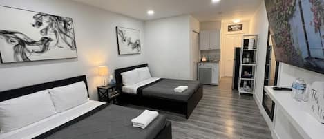 A modern hotel room with two beds, artwork on the walls, a kitchenette, and a large window.