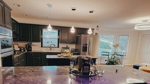 Une cuisine moderne avec des meubles de couleur sombre, un îlot en marbre et des luminaires suspendus.