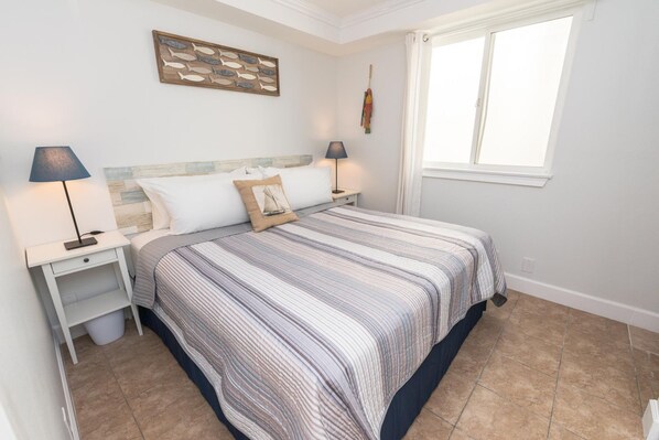 A neatly arranged bedroom with a bed, two bedside tables, a wall-mounted lamp, and a window with curtains.