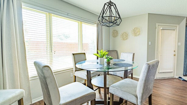 Un coin repas avec une table en verre entourée de quatre chaises, un luminaire suspendu et une plante en pot.