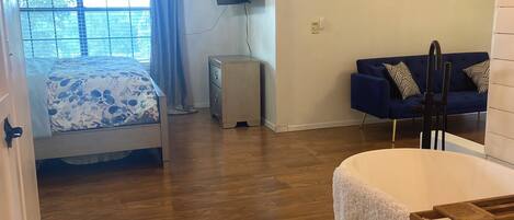 Una habitación con una cama, un escritorio, una silla, un televisor montado en la pared y una ventana con cortinas.