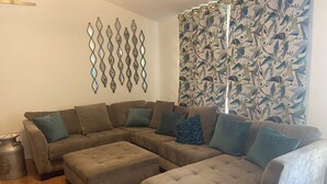 A sectional sofa with multiple cushions, a small ottoman, and a decorative wall piece. - The Ark!!! (Sulphur Rock)