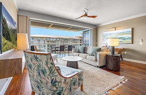 A spacious living room with a sofa, chairs, a coffee table, and a view of a building with balconies.