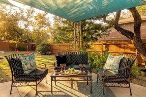 Eine Terrasse mit zwei Metallstühlen, einem Tisch und einem überdachten Bereich.