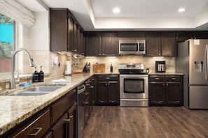Una cocina moderna con gabinetes de madera oscura, electrodomésticos de acero inoxidable, una encimera de granito y un horno empotrado.