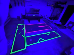 Ein Zimmer mit einem Bett, einem Schreibtisch und einem Spieltisch mit Neonkonturen.
