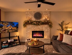 A living room with a fireplace, a television, and a coffee table with snacks and drinks. - Bring generations together, 5 bdrms, hot tub, fire pit and games. (San Antonio)