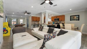 A spacious living area with a white leather sofa, a pool table, and ceiling fans.