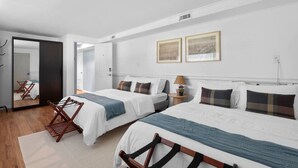 A modern hotel room with two beds, a mirror, a small table with a lamp, and a wooden chair.
