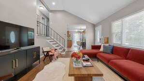 A modern living room with a large flat-screen TV, a red sofa, a wooden coffee table, and a staircase leading to an upper floor.