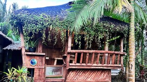 A wooden structure with a bench, surrounded by lush greenery and a thatched roof. - Spark Camp - Baler (Baler)