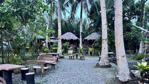An outdoor seating area with tables and chairs, surrounded by palm trees and greenery. - Spark Camp - Baler (Baler)