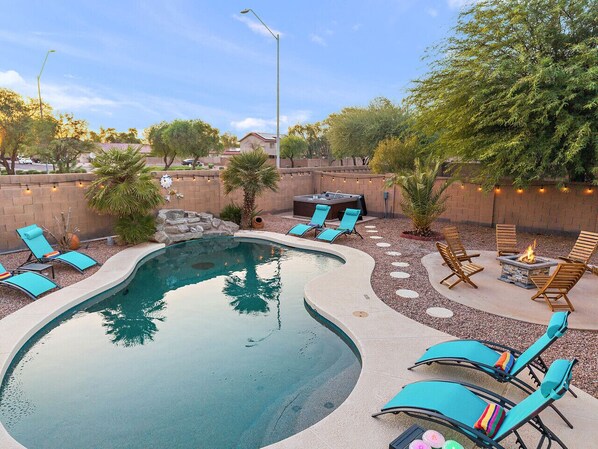 A swimming pool with blue lounge chairs and a fire pit area.