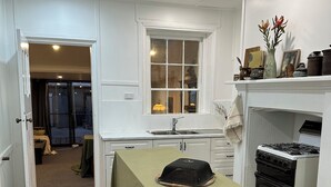 A kitchen with a dining table covered in a green tablecloth, a stove, and a window with curtains. - Atelier’s Den-Wood Fire Hot Tub, Centre Of Town (Beechworth)