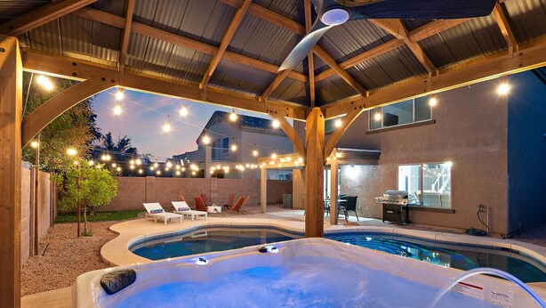 Un espace comprenant un jacuzzi et une piscine, agrémenté de poutres en bois, de guirlandes lumineuses et de mobilier d’extérieur.