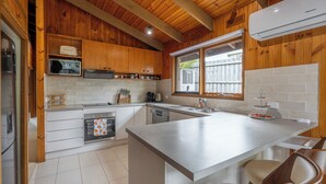 A modern kitchen with wooden cabinets, a central island, a dishwasher, and a window overlooking a backyard. - Spacious | Pet Friendly| Near Boat Ramp and Water (Clifton Springs)