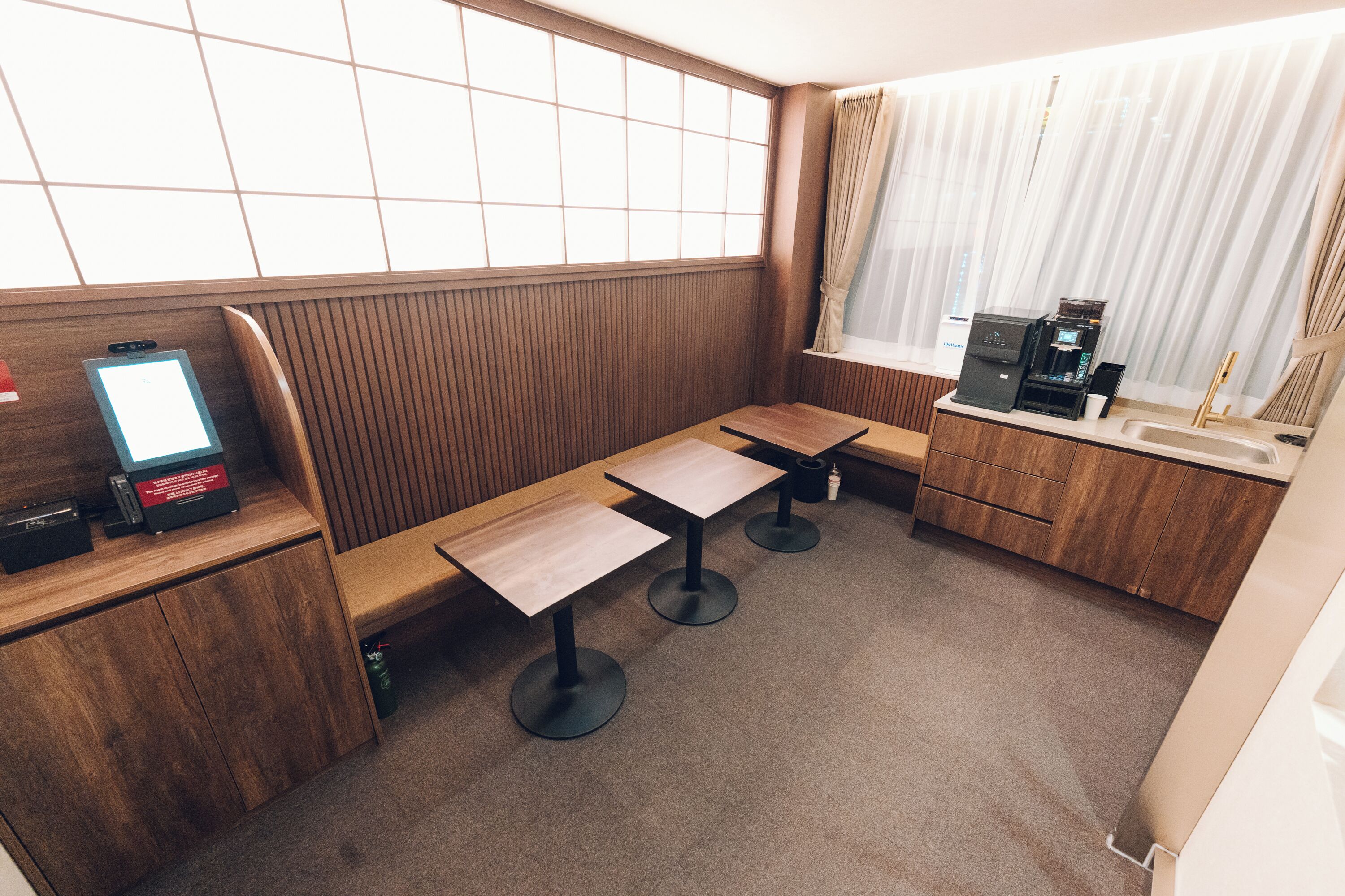 A compact hotel room with a wooden bench seating area, a small kitchenette, and a window with curtains.