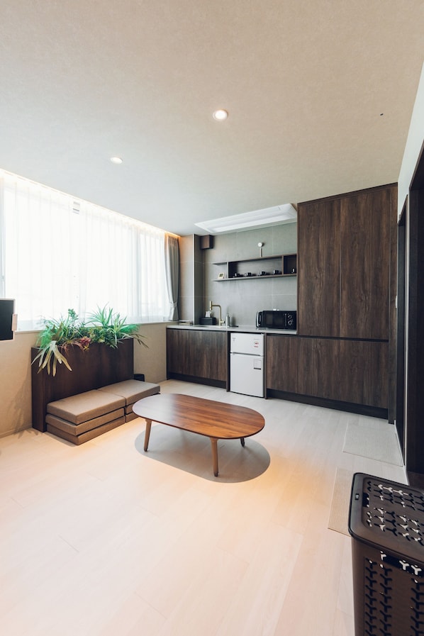 A modern kitchen with dark wood cabinets, a built-in microwave, and a small refrigerator. There is a wooden dining table and a bench in the living area. - Monthliv Gwangjang Market Hotel Stay (Seoul)