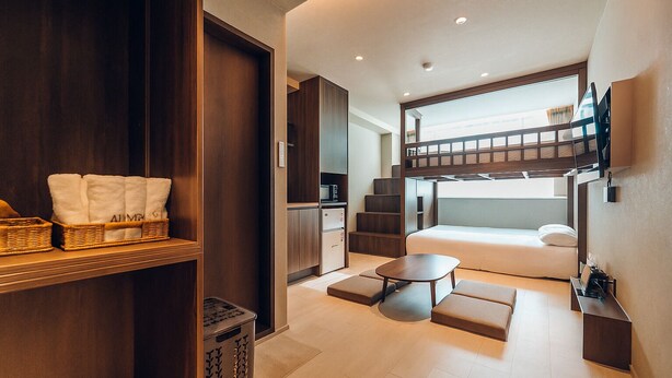 Una habitación de hotel moderna con literas, una kitchenette pequeña, un comedor y un ventanal grande que proporciona luz natural.