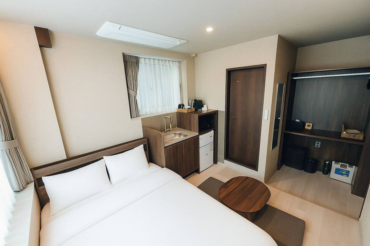 A hotel room with a bed, a small kitchenette, a private bathroom, and a TV.