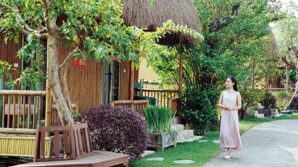A wooden bench and a thatched-roof building in a garden setting. - KST Linh Ky Moc (Quang Phu)